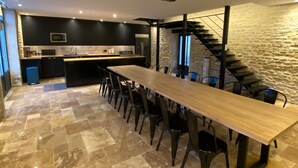 Eine moderne Küche mit einem langen Holztisch und Stühlen, einer Steinwand und einer Treppe.