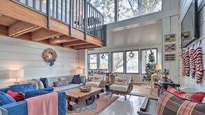 A spacious living room with a high ceiling, wooden beams, and large windows. There are two sofas, a coffee table, and a fireplace. - 'The Chalet on Sinclair' w/ Private Dock & Kayaks! (Eatonton)