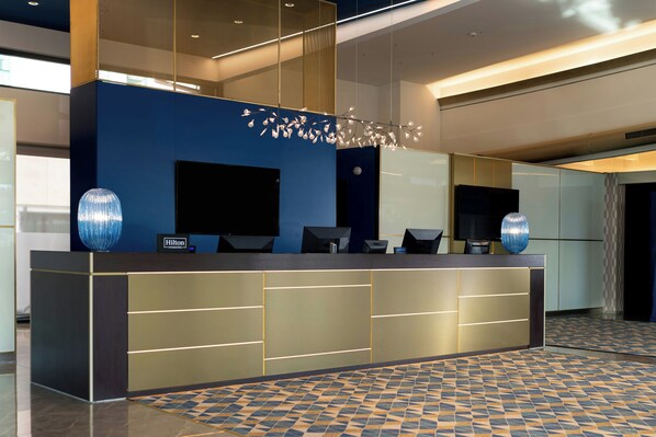 A modern reception desk with a flat-screen TV, a digital display, and a nameplate. - Doubletree BY Hilton Milan Malpensa (SOLBIATE OLONA)