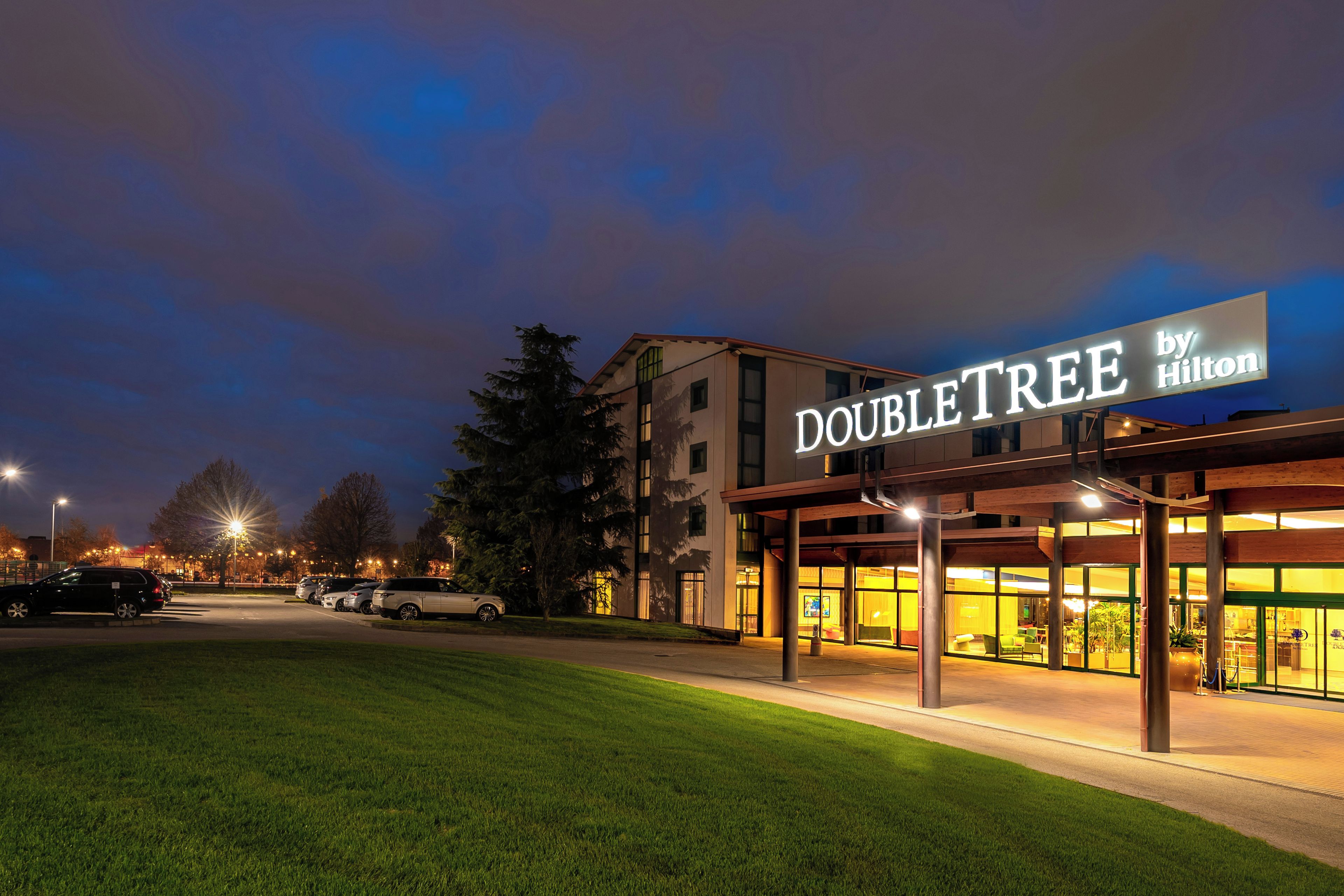 Un hôtel appelé « DOUBLETREE by Hilton », doté d’une façade moderne, d’un parking et d’une pelouse bien entretenue.