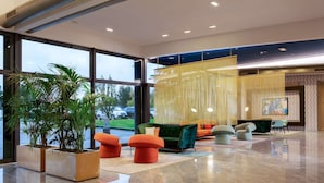 A spacious lobby with large windows, a central seating area with colorful chairs, and a large potted plant. - Doubletree BY Hilton Milan Malpensa (SOLBIATE OLONA)