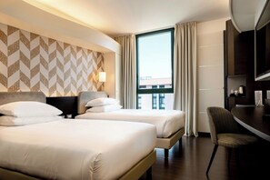 A hotel room with two beds, a desk, a chair, a TV, and a window with curtains. - Doubletree BY Hilton Milan Malpensa (SOLBIATE OLONA)