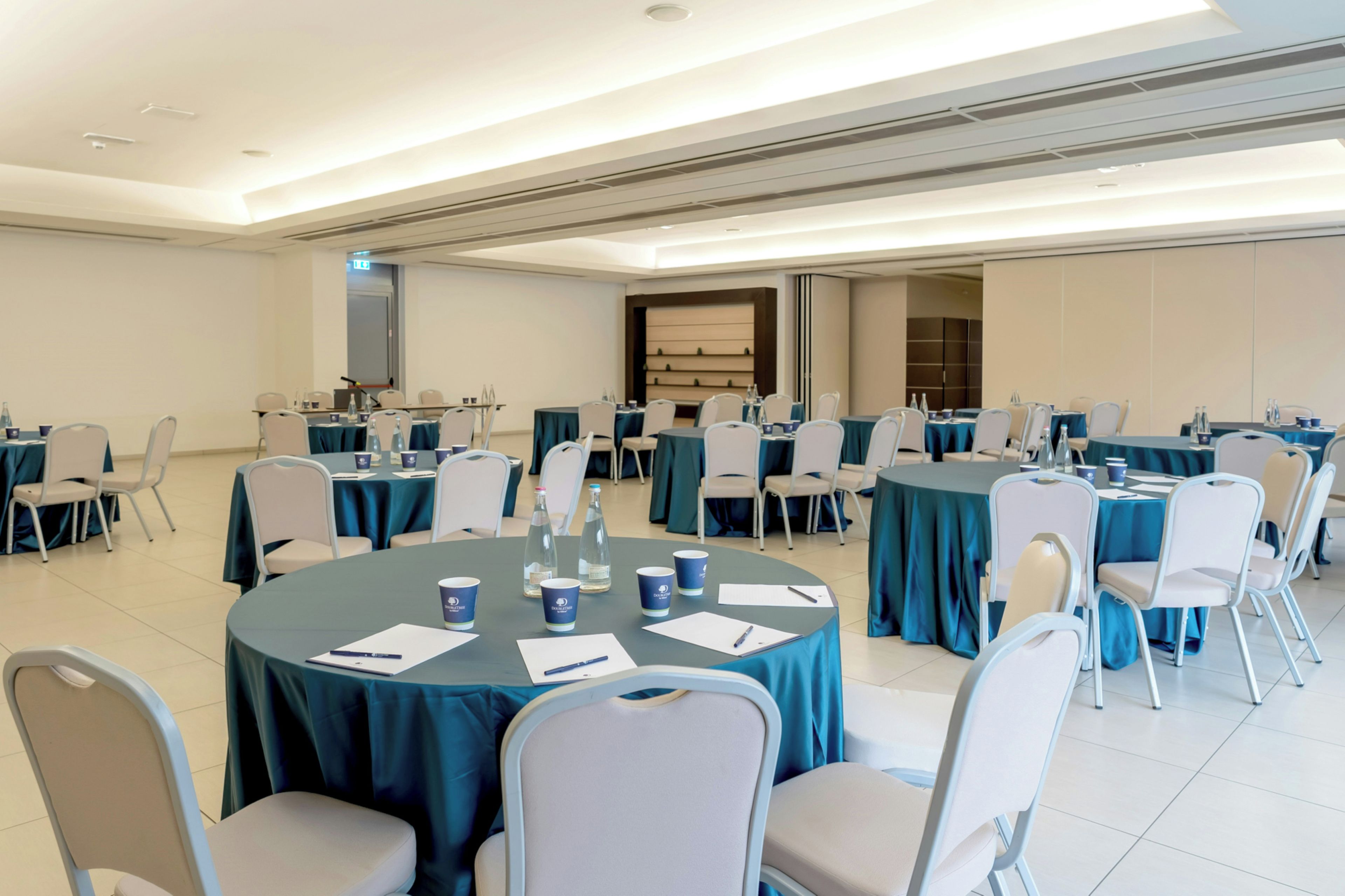 A conference room with multiple tables, chairs, and a projector screen.