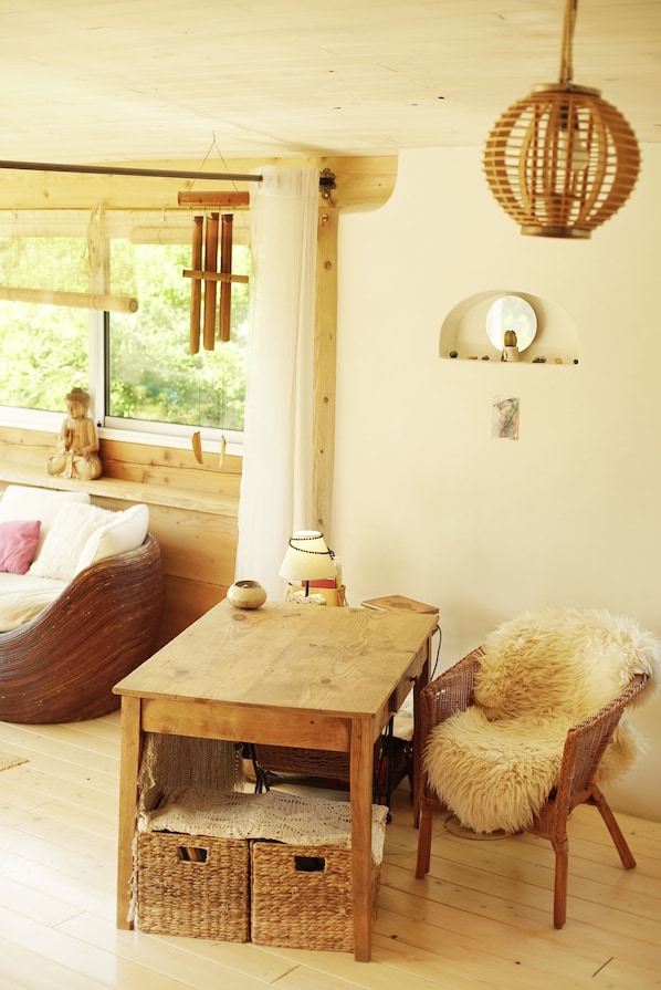 A cozy room with a wooden table, wicker furniture, and a large window with a view of greenery.