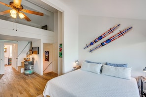Een slaapkamer met een groot bed, een plafondventilator, ski’s aan de muur en een rustieke ton.