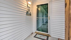 Fachada blanca con puerta de vidrio, felpudo y aplique de pared.