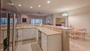 Una cocina moderna con una isla central, armarios blancos y un comedor con mesa y sillas de madera.