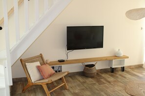 Sala de estar com um banco de madeira, uma cadeira de vime, uma televisão fixada na parede e uma cesta trançada no chão.