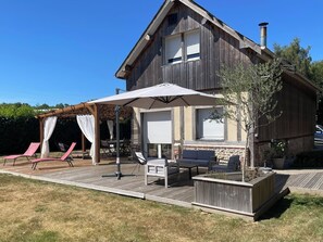 Une maison en bois à deux étages, dotée d’un patio couvert aménagé avec du mobilier d’extérieur et une pergola.