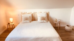 A neatly made bed with a wooden headboard, a bedside lamp, and a small table with a lamp and a basket.