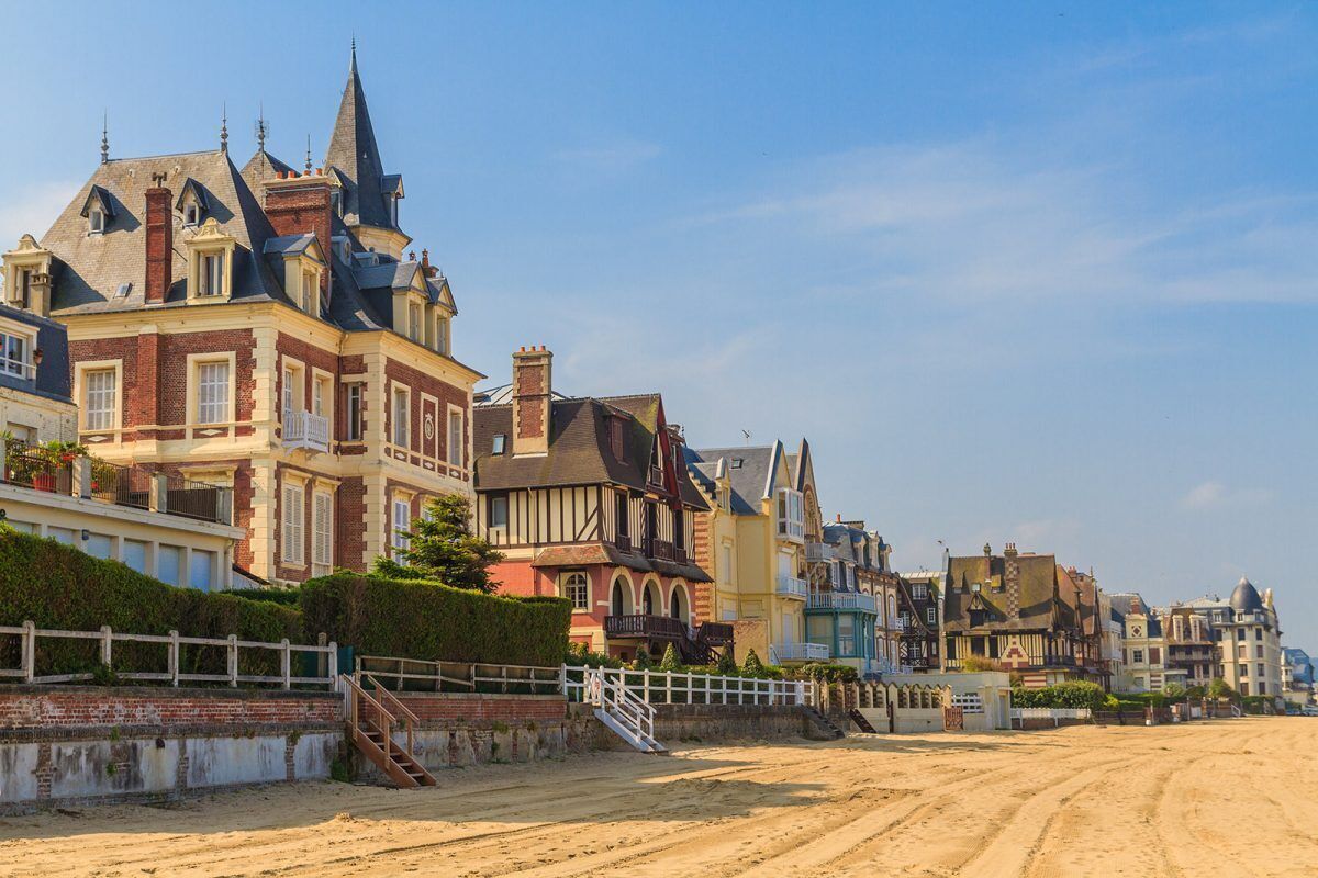 Une rue côtière bordée de bâtiments historiques, un sentier sablonneux et une clôture blanche.