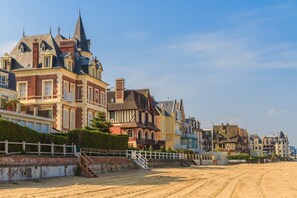 A coastal street with historic buildings, a sandy path, and a white fence.