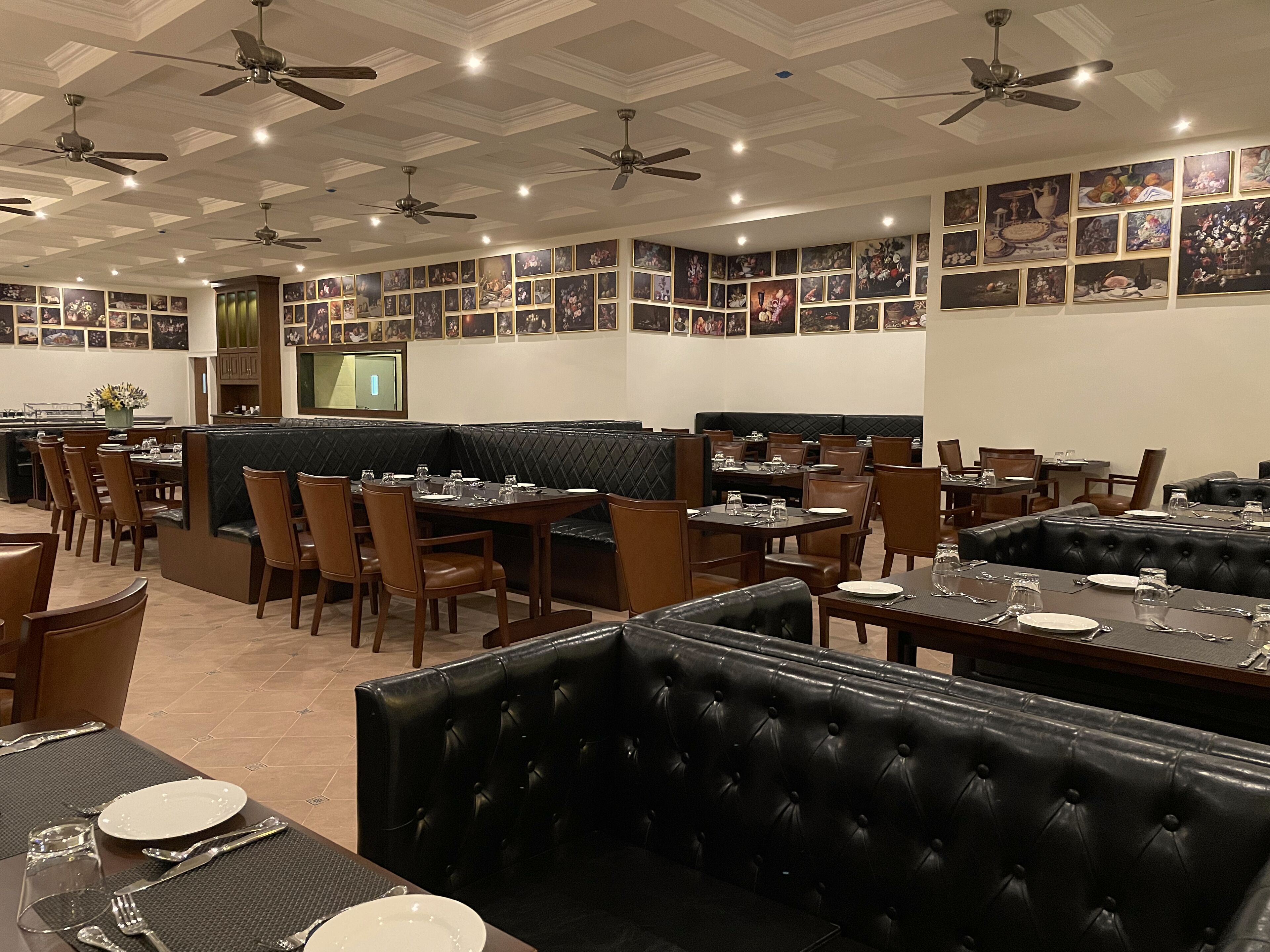 A restaurant with multiple dining areas, including booths and tables, with ceiling fans and wall-mounted artwork.