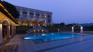 A large, multi-story hotel with a swimming pool, outdoor lighting, and a landscaped garden. - Montrose Golf Resort & Spa (Somvarpet)