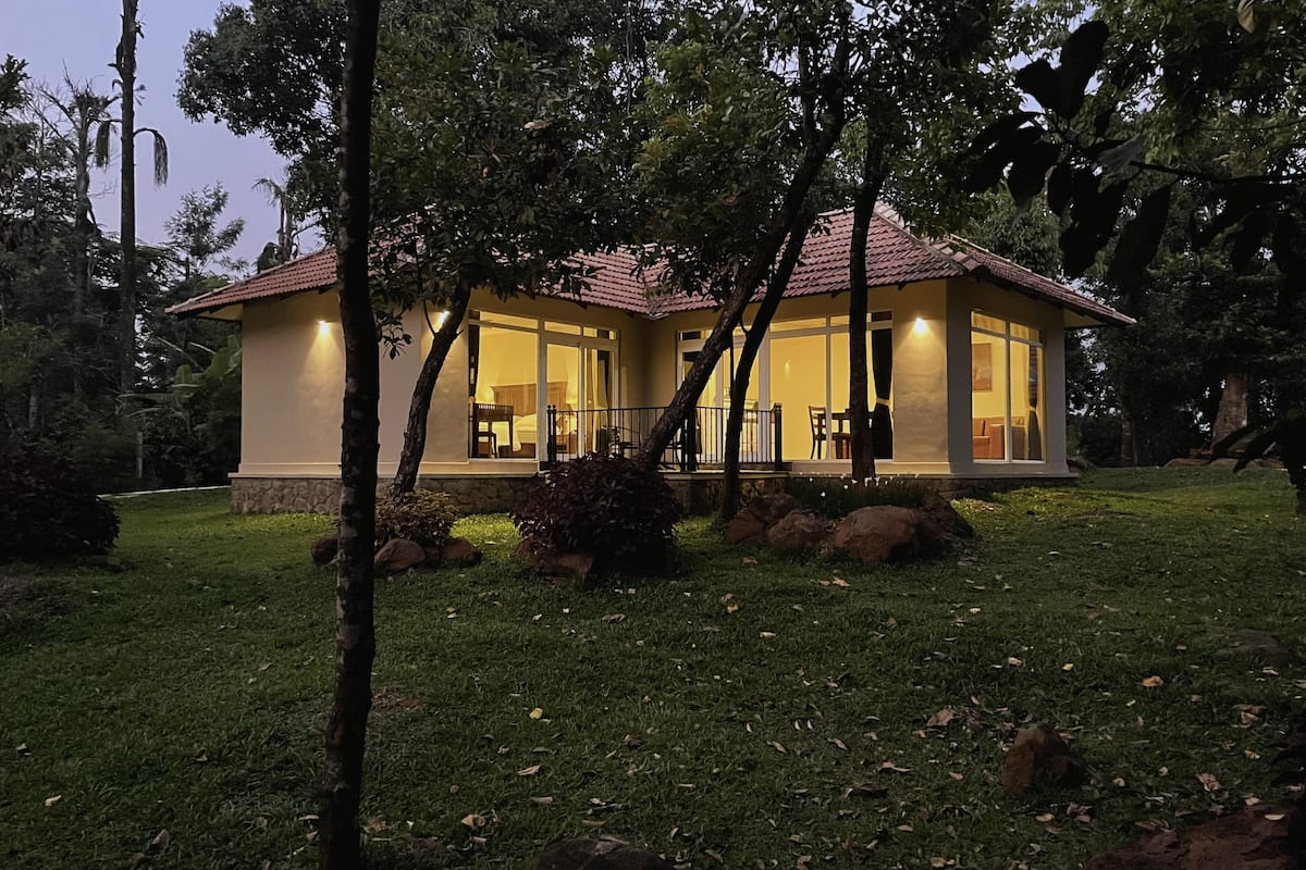 A two-story house with a red-tiled roof, large glass windows, and a well-maintained lawn.