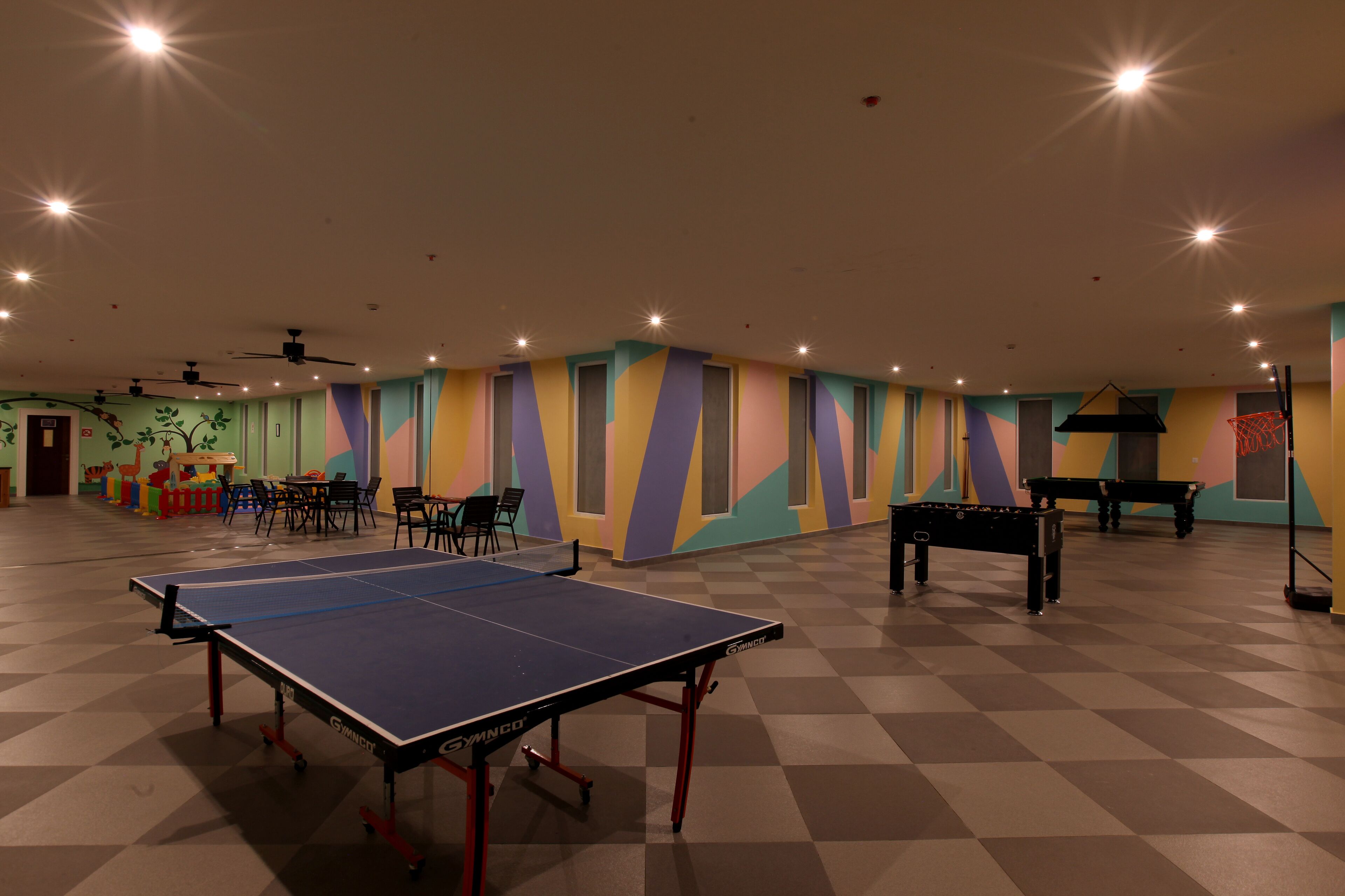 Un grand espace intérieur comprenant une table de ping-pong, un baby-foot et un panier de basket.