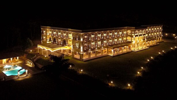 A large, illuminated hotel with multiple balconies and a swimming pool. - Montrose Golf Resort & Spa (Somvarpet)