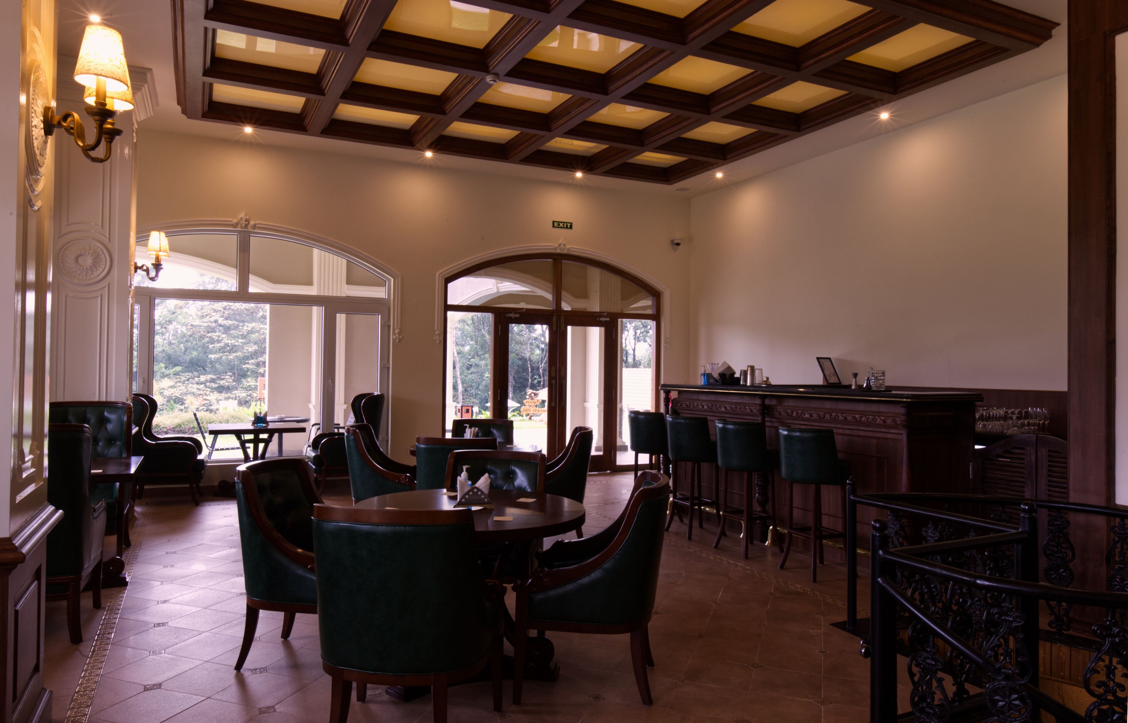 A spacious dining area with high ceilings and large windows, featuring a bar and multiple tables and chairs.