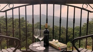 A balcony with a table set for two, featuring a bottle of wine, two wine glasses, a book, and a bouquet of flowers. - Montrose Golf Resort & Spa (Somvarpet)