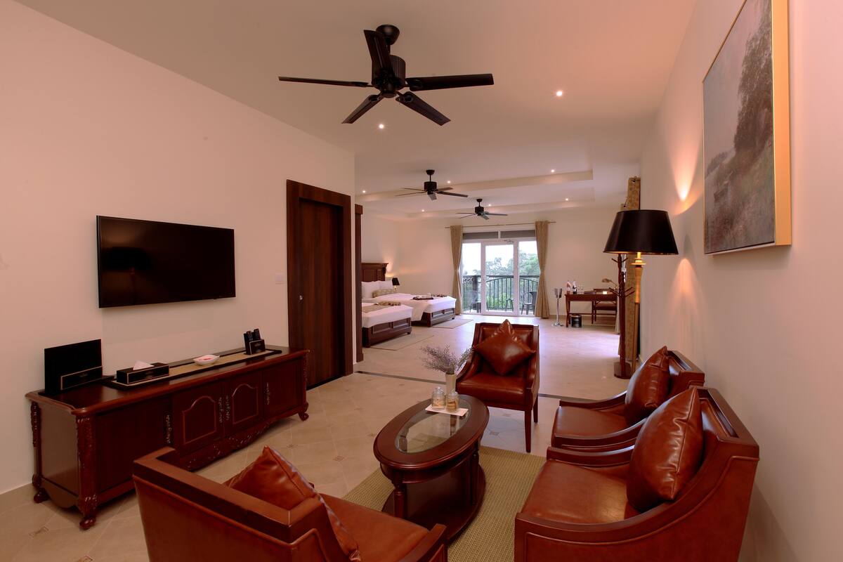 A spacious living area with a flat-screen TV, a wooden entertainment unit, leather sofas, a coffee table, and ceiling fans.