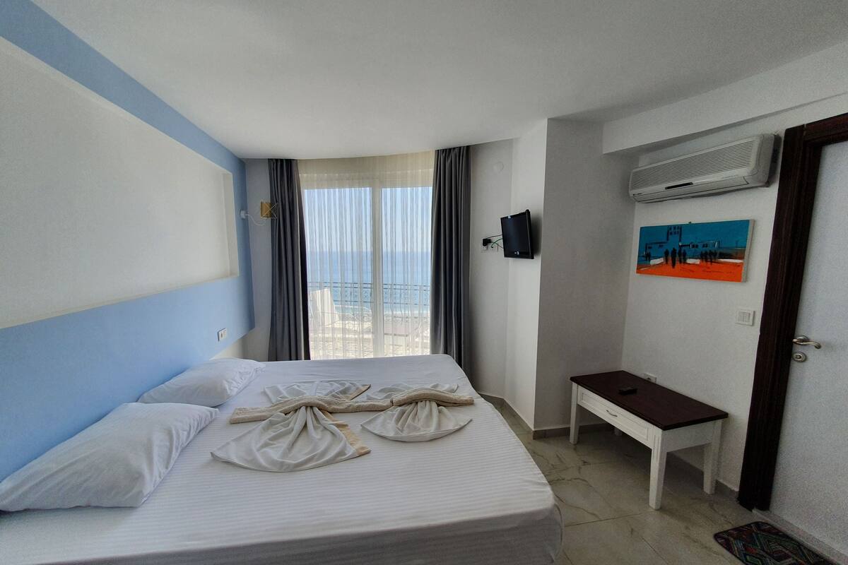 A hotel room with a bed, a small table, a TV, and a painting on the wall.