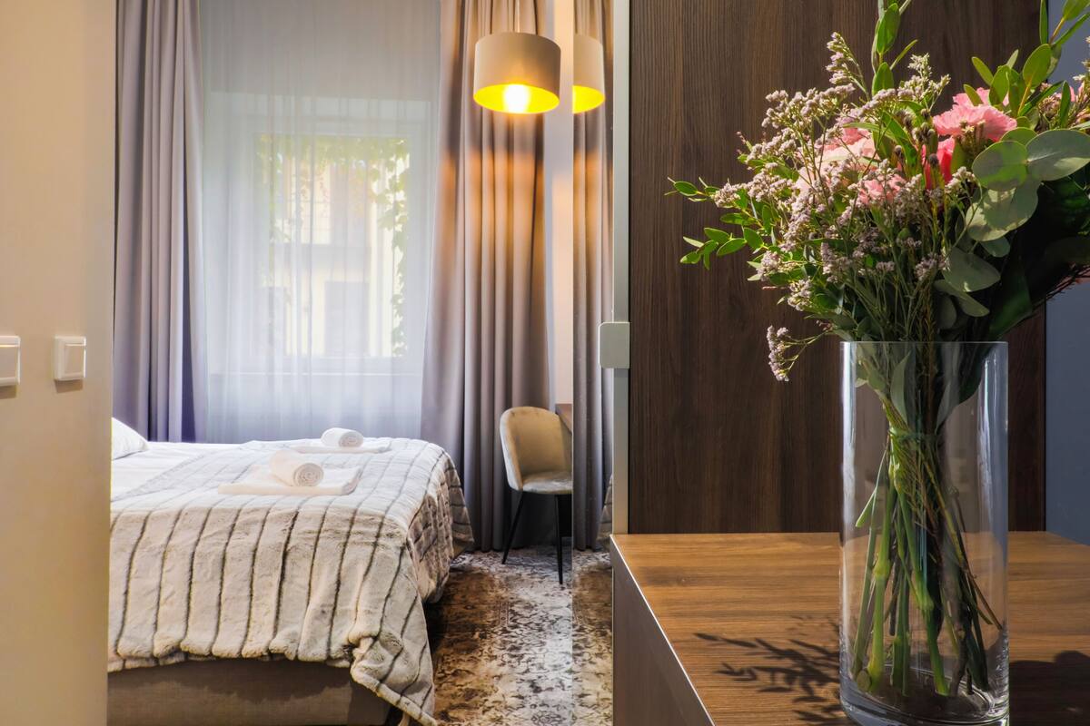 Een hotelkamer met een bed, een stoel, een houten tafel en een vaas met bloemen.