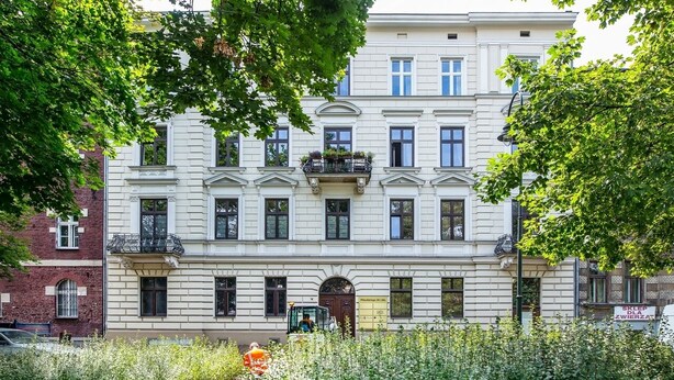 Un immeuble à plusieurs étages, de style architectural classique, doté d’une entrée centrale surmontée d’une arche décorative et de nombreuses fenêtres à chaque étage.