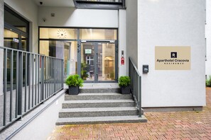 A hotel entrance with a staircase leading to the door, a clock above the door, and a sign for 'Aphthotel Cracovia Residence'.