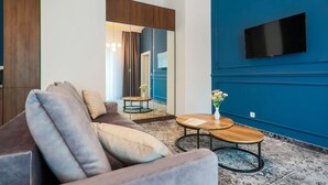Un salon moderne avec un canapé gris, une table basse en bois et un mur d’accent bleu sur lequel est fixée une télévision.