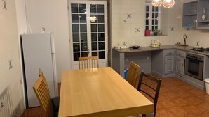 Cocina compacta con zona de comedor, que incluye una mesa de madera, sillas, un refrigerador, una estufa y lámparas colgantes.