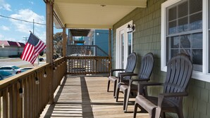 A wooden deck with chairs, a railing, and American flags. - Salty Pause 3 Bedroom Home in Kill Devil Hills (Kill Devil Hills)
