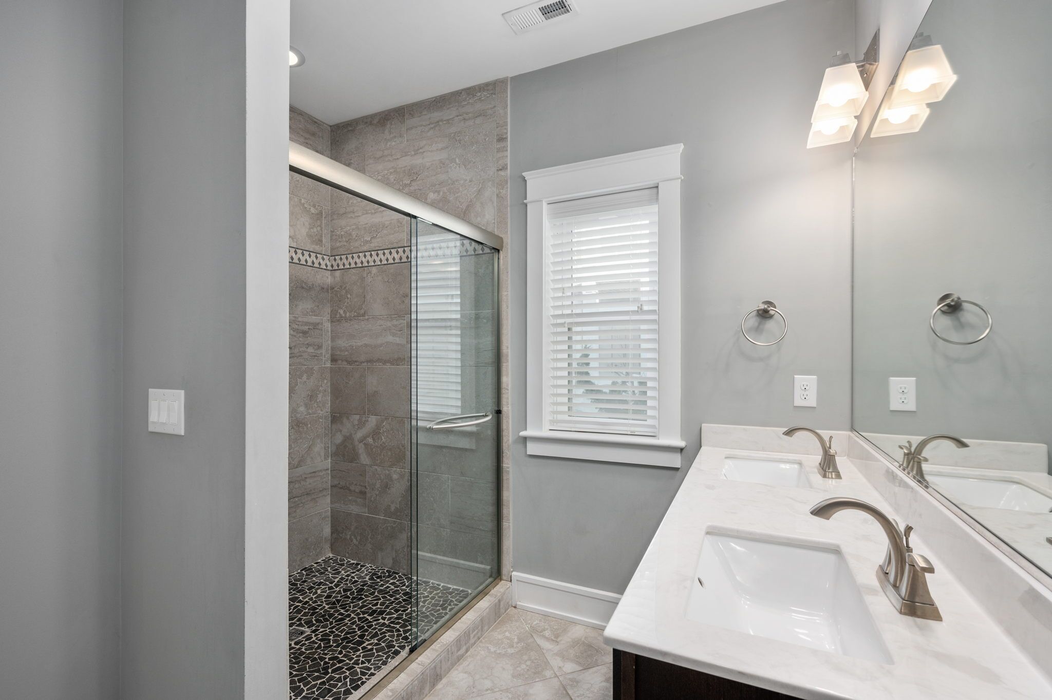 A modern bathroom with two sinks, a glass shower enclosure, and a window with blinds.