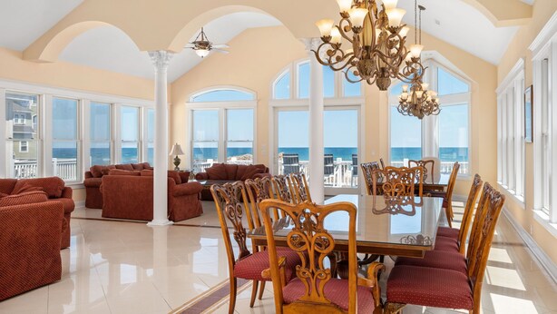 A spacious dining area with a large table and ornate chairs, overlooking a scenic ocean view. - Imperial Palace Pool + Oceanfront + Pets Stay Free (Kill Devil Hills)