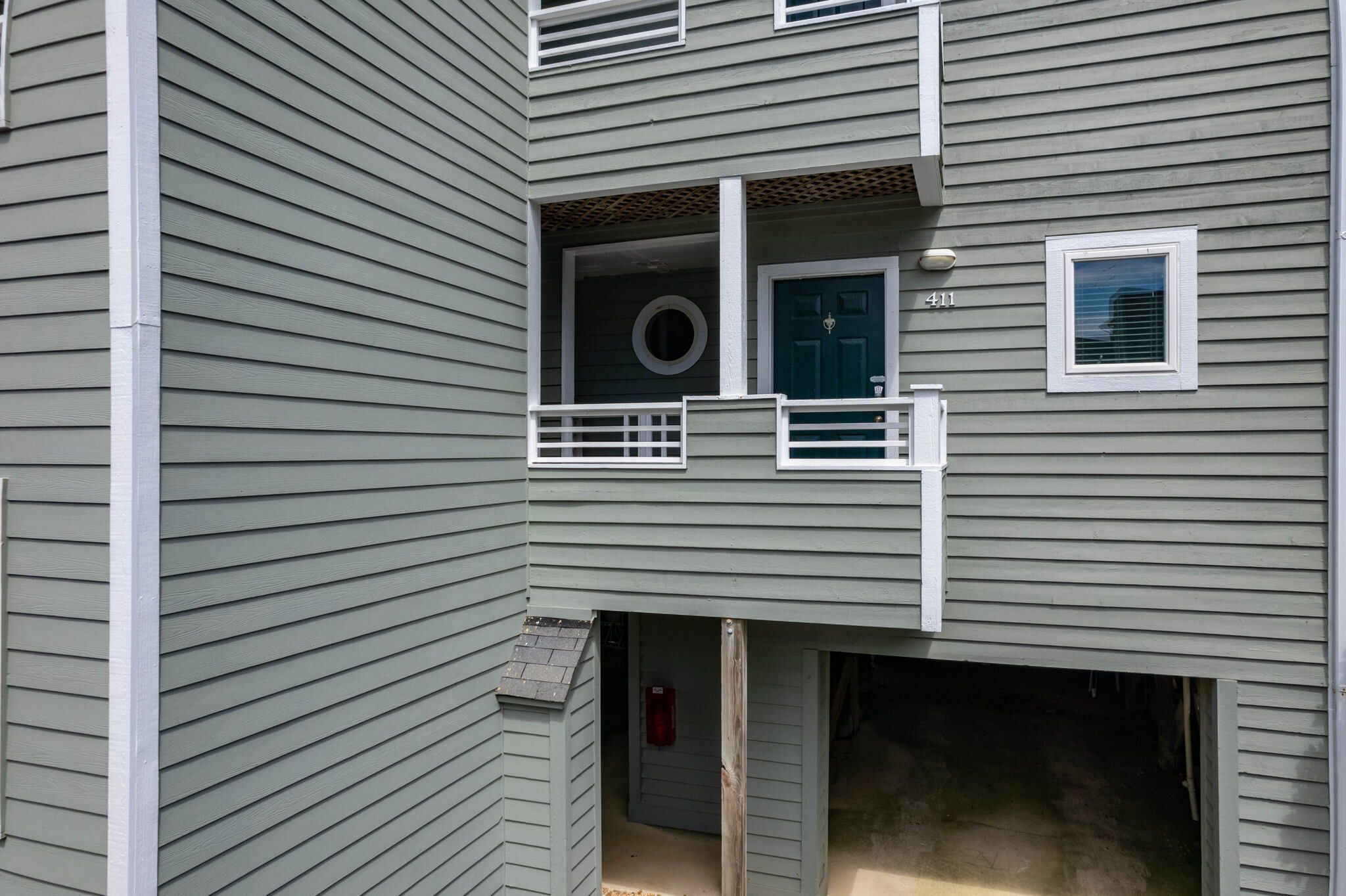 Un edificio de varios pisos con un balcón, una puerta de garaje y un ventanal pequeño.