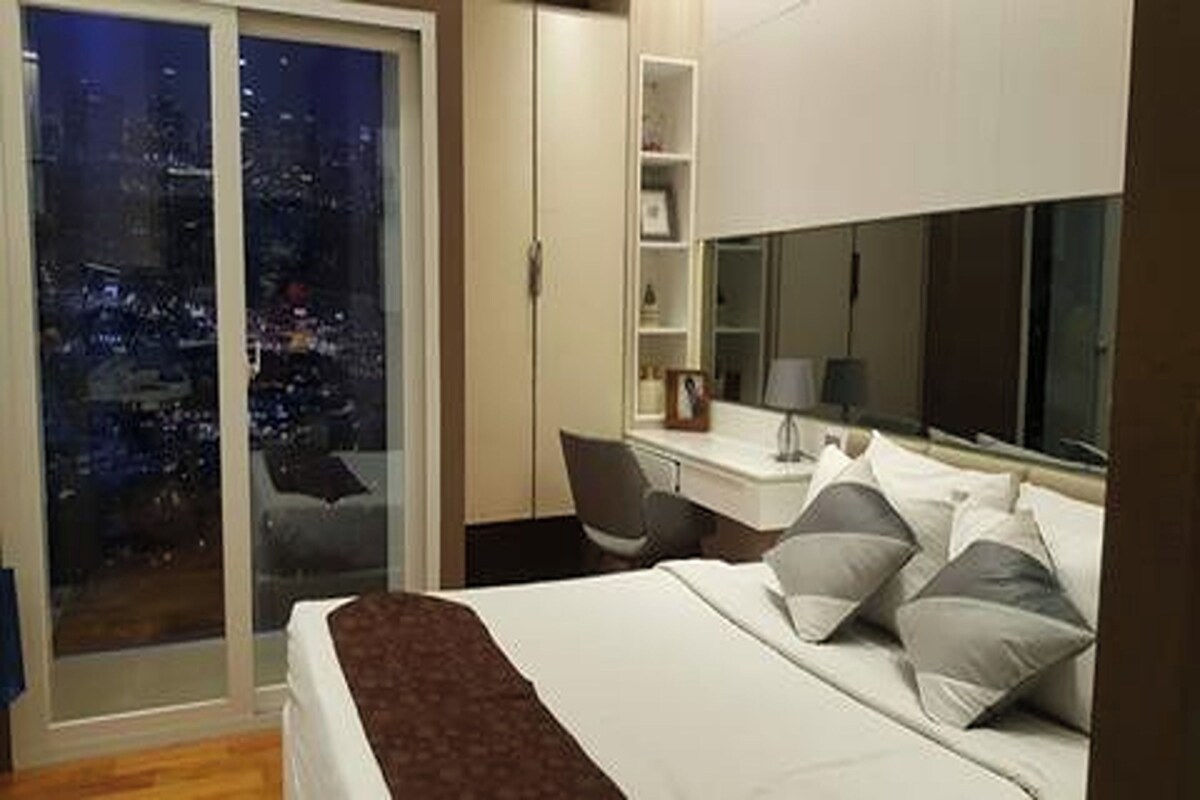 Ein Hotelzimmer mit Bett, Schreibtisch und Blick auf die beleuchtete Stadt bei Nacht.