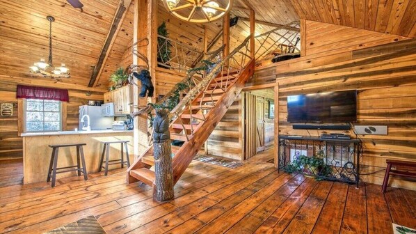 A wooden cabin interior with a staircase, kitchen, and living area.