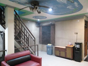 A room with a staircase, a ceiling fan, a trash bin, a cabinet, and a water dispenser. - Hotel Alifah 1 by Zuzu (Tangerang)
