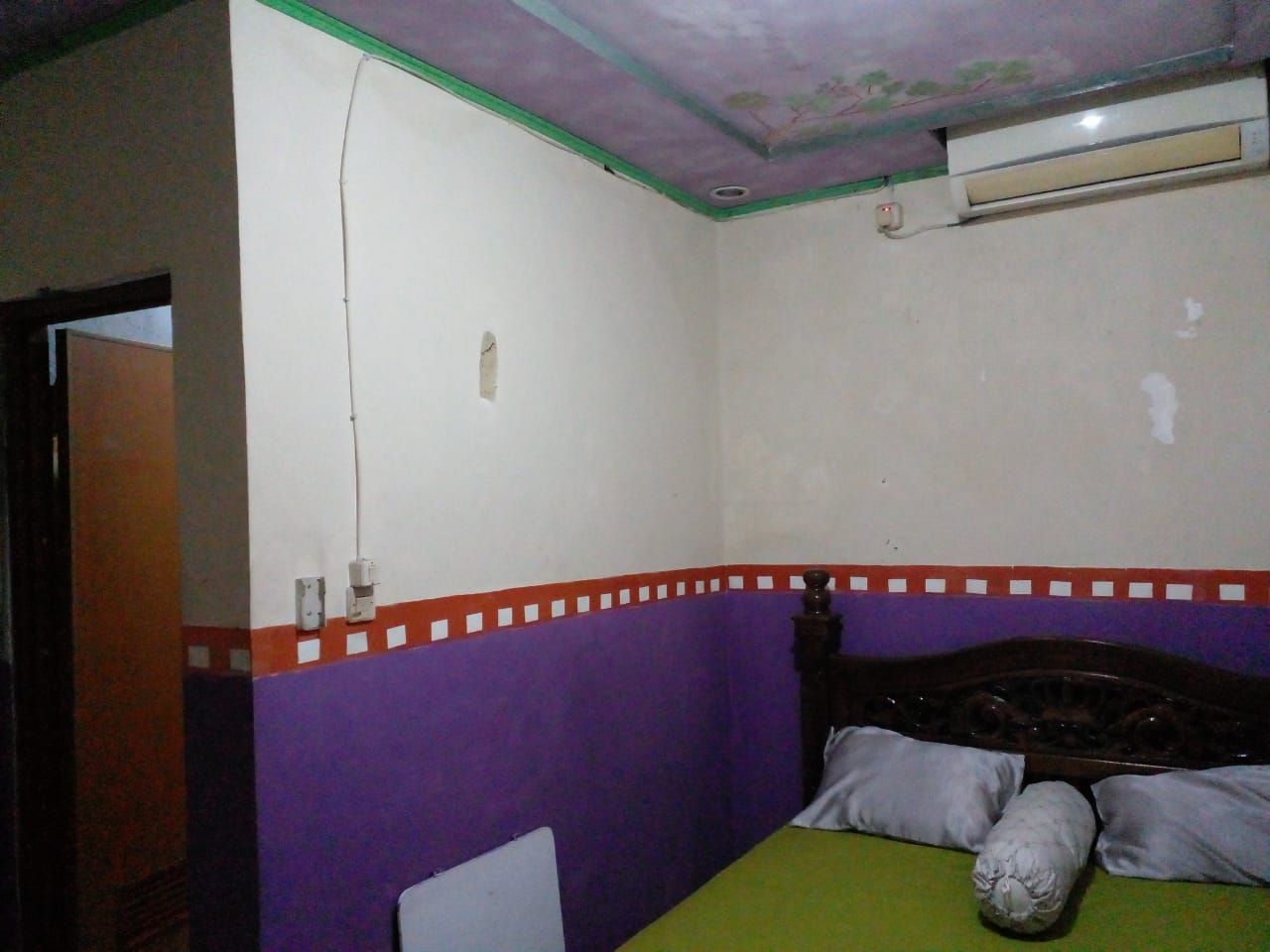 Quarto com cama, parede roxa e branca e cabeceira de madeira.