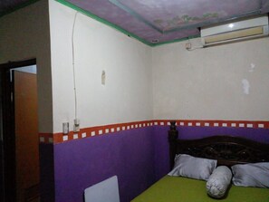 Una habitación con una cama, pared morada y blanca, y cabecero de madera.