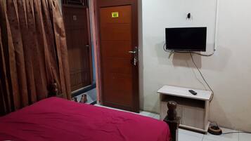 A room with a bed, a television mounted on the wall, a wooden door, and a curtain.