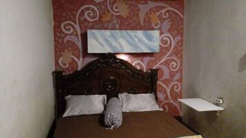 A bedroom with a wooden bed, two pillows, a blanket with cartoon characters, a wall-mounted air conditioner, and a small bedside table.
