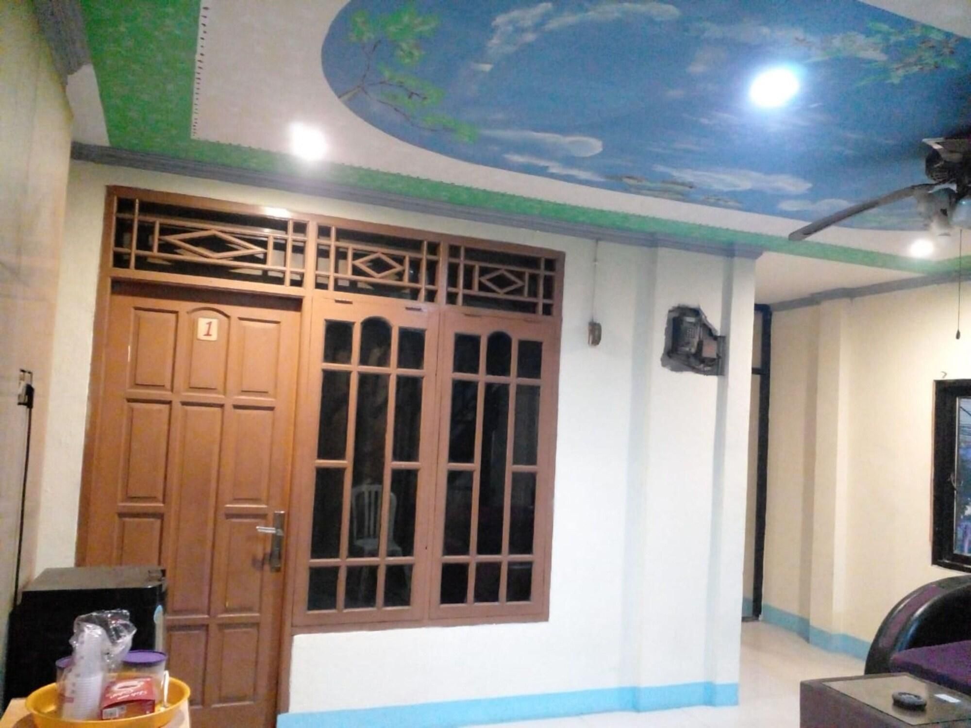 Quarto com porta de madeira grande, janela com grade e um ventilador de teto, além de uma televisão.