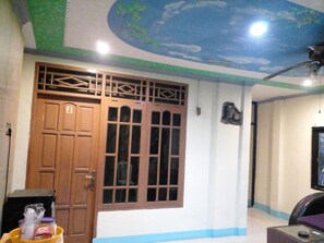 Una habitación con una puerta de madera grande, una ventana con diseño de cuadrícula, un ventilador de techo y un televisor.