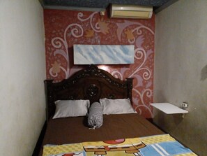 A small bedroom with a wooden bed, two pillows, a blanket, and a wall-mounted air conditioner. - Hotel Alifah 1 by Zuzu (Tangerang)
