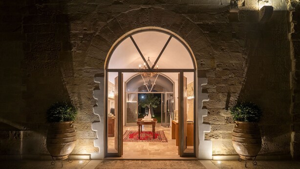 An arched entrance with a red rug leading to a table and chairs, flanked by potted plants. - Dimora Oru (Lecce)