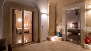 A room with a stone wall, a bed, and a glass door leading to another room. - Dimora Oru (Lecce)