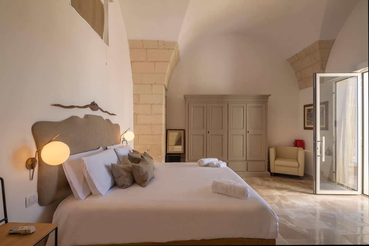 Un dormitorio con una cama grande, una mesita de noche, una lámpara de pared, un armario y una puerta corrediza de vidrio que da a un balcón.