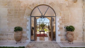 An entrance with a stone wall, a glass door, and two potted plants. - Dimora Oru (Lecce)