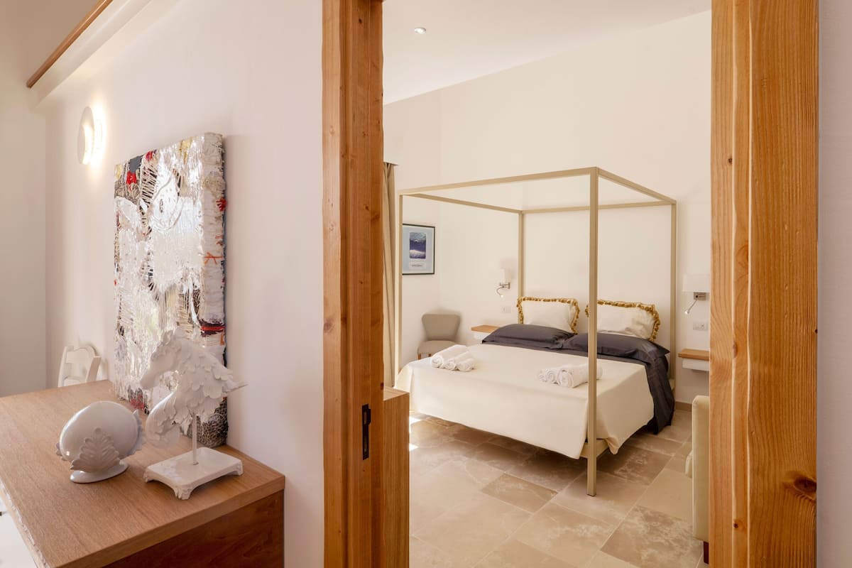 Un dormitorio con una cama con dosel, un escritorio de madera con un adorno y una obra de arte en la pared.