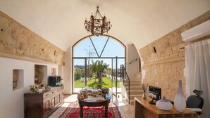 A spacious room with a large arched window, a chandelier, a wooden desk, and a red patterned rug. - Dimora Oru (Lecce)